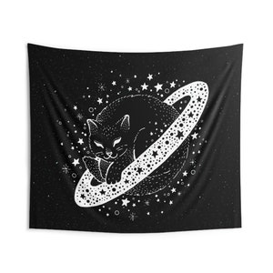 May include: Black and white tapestry featuring a sleeping cat inside a planet with a star-studded ring. The background is a dark starry sky. The cat is detailed with a whimsical design, creating a celestial theme.