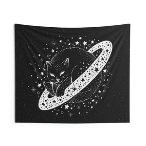 May include: Black tapestry featuring a white illustration of a cat sleeping on a planet with a dotted ring. The background is a starry night sky with white stars and dots. The cat is detailed with white outlines.