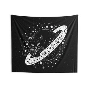 May include: Black tapestry featuring a white illustration of a cat sleeping on a planet with a star-studded ring. The background is black with white stars and dots. The cat is detailed with a smiling face and a relaxed pose. The tapestry is rectangular.