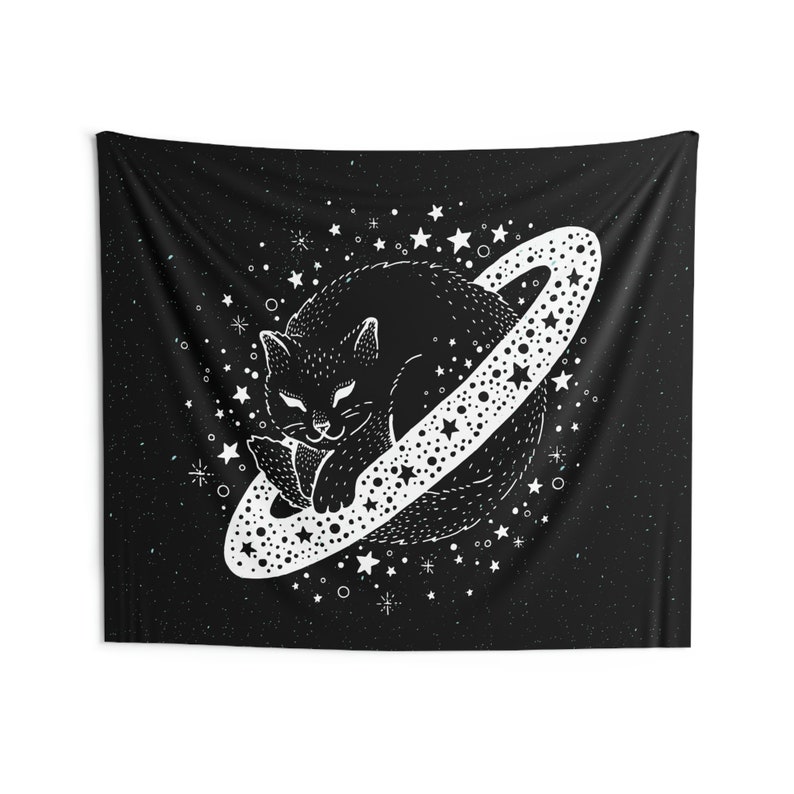 May include: Black tapestry featuring a white illustration of a cat sleeping on a planet with a star-studded ring. The background is black with white stars and dots. The cat is detailed with a smiling face and a relaxed pose. The tapestry is rectangular.