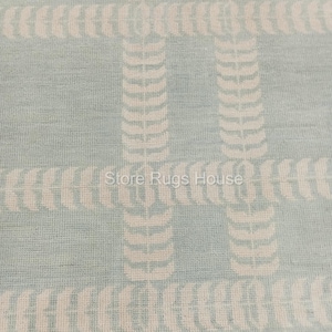 May include: A light blue rug with a white geometric pattern. The pattern is made up of repeating shapes that resemble leaves.
