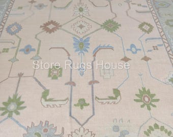 May include: A cream-colored rug with a geometric pattern in shades of blue, green, and brown. The rug has a border with a repeating pattern of triangles.