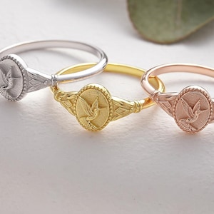 May include: Three silver, gold, and rose gold rings with a dove design. The rings are on a white surface.