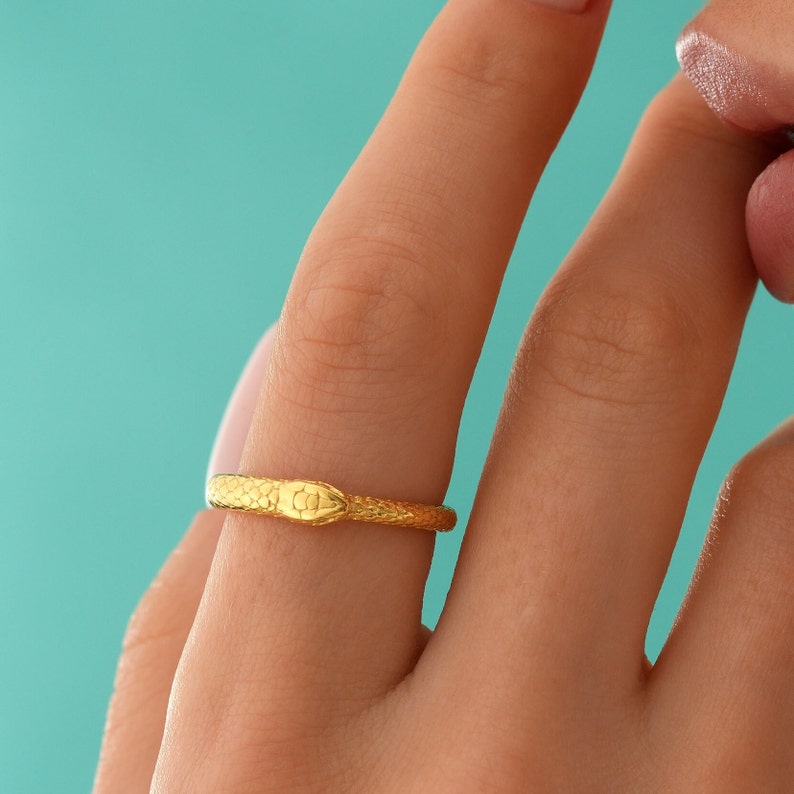 May include: A gold snake ring with a textured finish. The ring is worn on a finger.