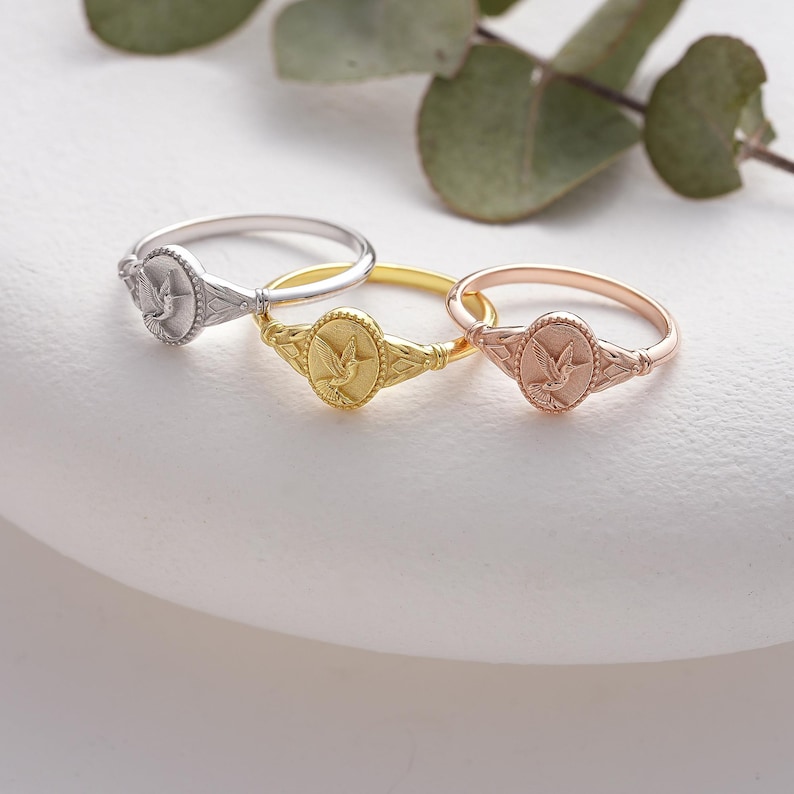 May include: Three silver, gold, and rose gold rings with a dove design. The rings are on a white surface.