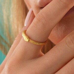 May include: A gold snake ring with a textured finish. The ring is worn on a finger.