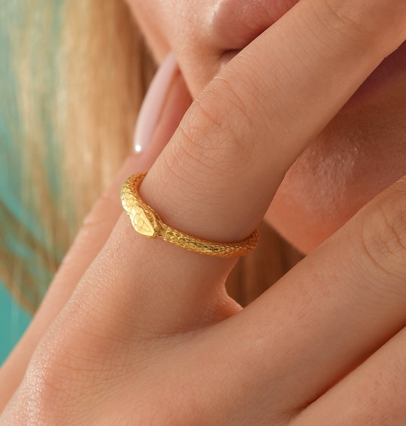 May include: A gold snake ring with a textured finish. The ring is worn on a finger.