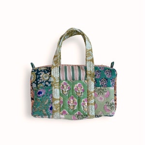 Puede incluir: Un bolso tote patchwork con una variedad de estampados florales y a rayas en tonos verdes, rosas y oliva. El bolso tiene dos asas y forma rectangular. El bolso está hecho de tela acolchada.