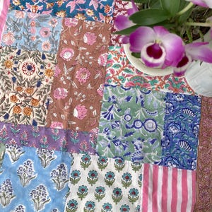 May include: A patchwork textile with diverse floral patterns in blue, pink, green, and brown. The design incorporates stripes and floral motifs, creating a vibrant and colourful display. The textile is likely a quilt or decorative fabric.
