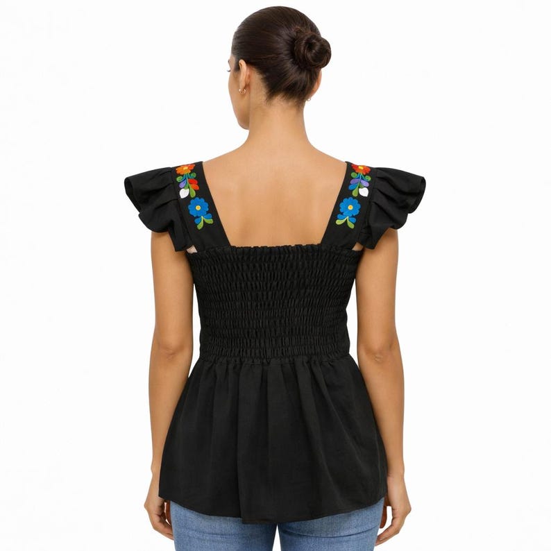 May include: Black top with floral embroidery on the shoulder straps. The top features a square neckline, ruffled sleeves, and a smocked bodice. The floral embroidery includes blue, orange, and white flowers. The bottom of the top has a flared design.