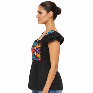 May include: Black embroidered top with a square neckline and ruffled sleeves. The top features a vibrant floral design in red, yellow, blue, purple, and green. The garment has a peplum style and is made of a dark fabric.