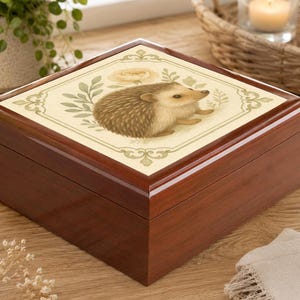 Peut inclure: Une boîte à bijoux en bois avec un dessus décoratif représentant une illustration de hérisson. La boîte est de couleur marron foncé avec une finition brillante. Le dessus a un fond crème avec des accents floraux et de feuilles.