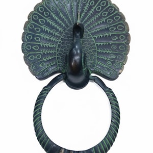 Op de afbeelding: Een decoratieve pauwenhanddoekring in een donker bronzen afwerking met groene accenten. De staartveren van de pauw zijn uitgespreid en de ring is ontworpen om een handdoek vast te houden. Het ontwerp is gedetailleerd en sierlijk.