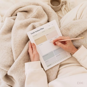 May include: A white Goal Action Plan paper sheet with sections for goal statement, start date, end date, reward, action plan, due date, potential obstacles, notes, and reflection, featuring pastel colored boxes and a light pink pencil.