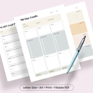 Könnte beinhalten: Eine 90-Tage-Ziel- und SMART-Ziel-Planervorlage auf weißem Papier mit beigen, grauen und pfirsichfarbenen Akzenten. Die Blätter enthalten Abschnitte für Fokus, Start- und Enddaten, Handlungsschritte und Fortschrittsanzeigen, begleitet von einem hellblauen Stift.