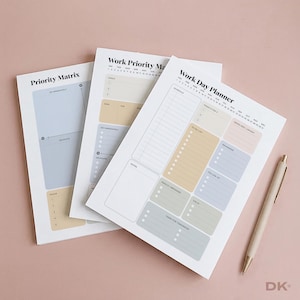 May include: Three white paper planner sheets with pastel-colored sections for organization. The sheets feature headings like Work Day Planner, Work Priority Matrix, and Priority Matrix, with sections for schedules, to-do lists, and goals, accompanied by a beige pen.