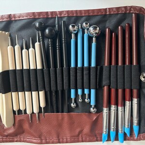 May include: A brown leather case with a black interior holds a variety of tools for sculpting and crafting. The tools include wooden, metal, and plastic implements with different shapes and sizes.