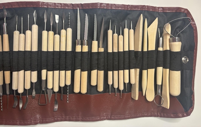 Pode incluir: Um conjunto de 25 ferramentas de cer&acirc;mica em um rolo de couro marrom. As ferramentas s&atilde;o feitas de madeira e metal e s&atilde;o usadas para moldar e esculpir a argila.