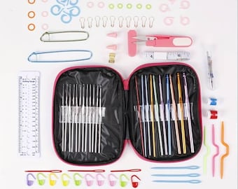 May include: A pink carrying case with a set of crochet hooks and knitting needles. The case is open and the hooks and needles are visible. There are also various other crochet supplies, including stitch markers, a measuring tape, and a pair of scissors.