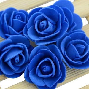 May include: Five blue foam roses, each with a slightly different shape and size, are arranged on a wooden surface.