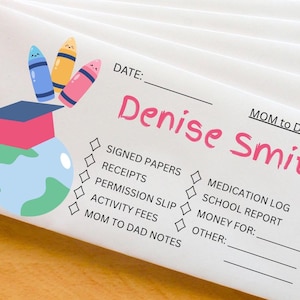 Op de afbeelding: Witte enveloppen met roze en zwarte tekst met de tekst "Denise Smith" en "MOM to DAD". De enveloppen hebben een kleurrijke illustratie van een afstudeerhoed over een wereldbol en drie kleurpotloden. De enveloppen hebben selectievakjes en lijnen voor notities.