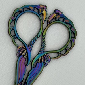 May include: A pair of iridescent scissors with a decorative floral design. The handles are intricately cut and feature a rainbow-like finish.