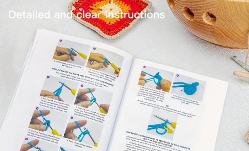 K&ouml;nnte beinhalten: Offenes Buch mit H&auml;kelanleitungen, das Schritt-f&uuml;r-Schritt-Fotos f&uuml;r eine Magic-Ring-Technik zeigt. Ein farbenfrohes H&auml;kelquadrat und eine Holzschale sind sichtbar. Der Text lautet "Detaillierte und klare Anweisungen".