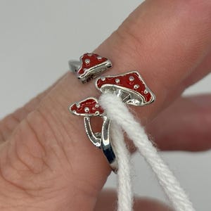 Könnte beinhalten: Ein silberner Ring mit zwei roten und weißen Pilz-Anhängern. Der Ring ist verstellbar und kann an jedem Finger getragen werden.