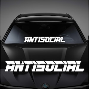 Könnte beinhalten: Ein schwarzes Auto mit einem weißen "ANTISOCIAL" Aufkleber auf der Windschutzscheibe und einem weißen "ANTISOCIAL" Aufkleber auf der vorderen Stoßstange.