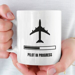 May include: White ceramic mug with a black airplane silhouette and a progress bar that reads "Pilot in Progress".