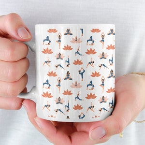 May include: White ceramic mug featuring a pattern of women in various yoga poses and orange lotus flowers.