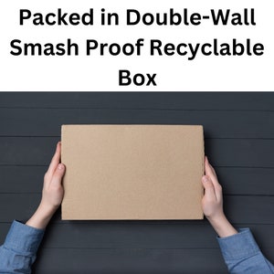 以下が含まれることがあります： 黒い木製の表面に、「Packed in Double-Wall Smash Proof Recyclable Box」という文字が書かれた茶色の段ボール箱。