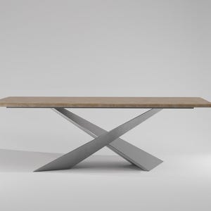Puede incluir: Una mesa de comedor moderna con una tapa de madera marrón claro y una base de metal plateado. La base tiene forma de X y está hecha de dos piezas de metal que se cruzan en un ángulo de 90 grados.