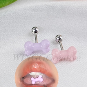 May include: Three silver barbell earrings with pink and purple bone-shaped charms. The charms have a textured surface. The earrings are shown on a white background.