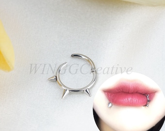 May include: Silver lip ring with five sharp points. The ring is shown on a model's lower lip.