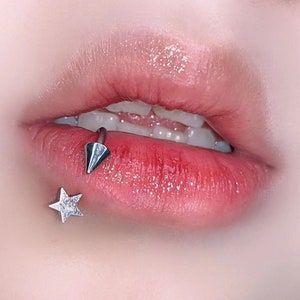 Peut inclure: Gros plan sur les l&egrave;vres d'une personne avec un piercing labial argent&eacute; en forme d'&eacute;toile et d'une pointe.