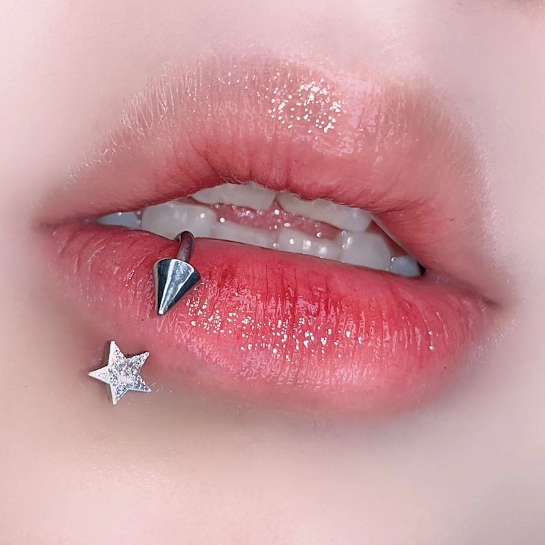 Peut inclure: Gros plan sur les l&egrave;vres d'une personne avec un piercing labial argent&eacute; en forme d'&eacute;toile et d'une pointe.