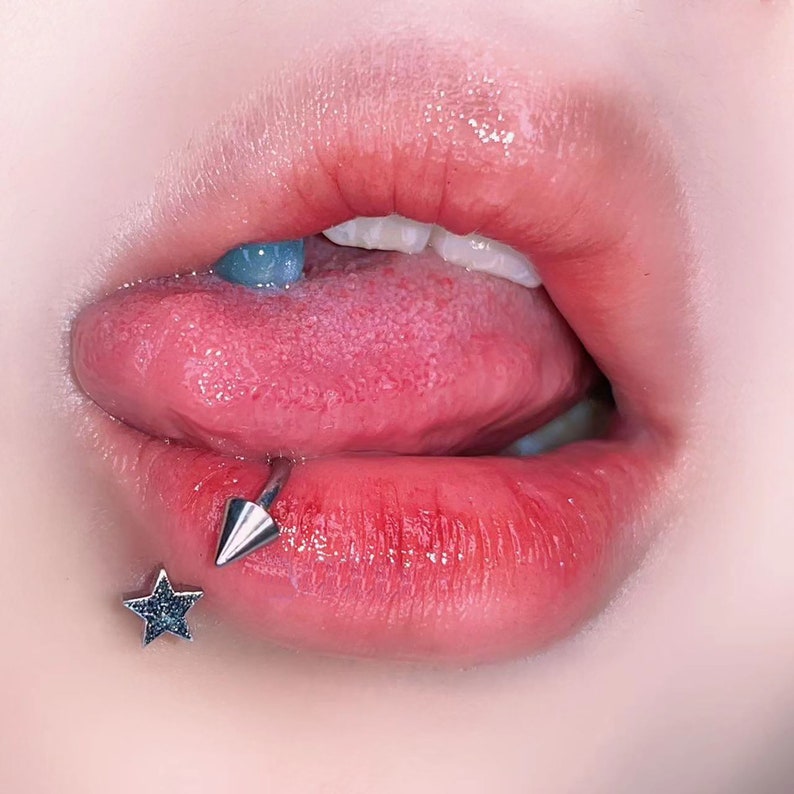 Peut inclure: Gros plan sur la bouche d'une personne avec un piercing &agrave; la l&egrave;vre en forme d'&eacute;toile argent&eacute;e. Le piercing a une petite pointe pointue et est plac&eacute; sur la l&egrave;vre inf&eacute;rieure.