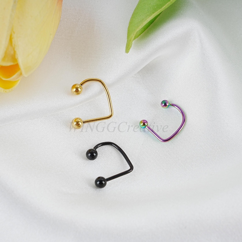 Puede incluir: Tres anillos de nariz con bolas de diferentes colores. Los anillos son de metal y tienen forma de U. Las bolas son doradas, negras y arco&iacute;ris.