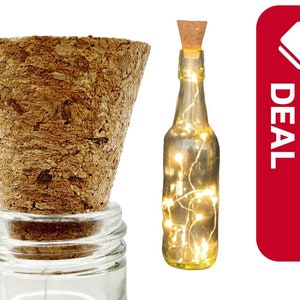 May include: A clear glass bottle with a cork top filled with white fairy lights. The bottle is sitting on a wooden surface.  The image also includes a cork top for a bottle.