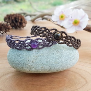Peut inclure: Deux bracelets en macramé avec des perles de pierres précieuses. Le bracelet du haut a une perle brun foncé et le bracelet du bas a une perle violette.