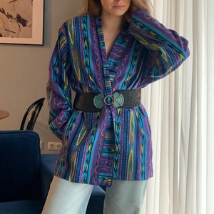 May include: A blue and purple patterned jacket with a black belt and a turquoise and silver buckle. The jacket has long sleeves and a V-neck.