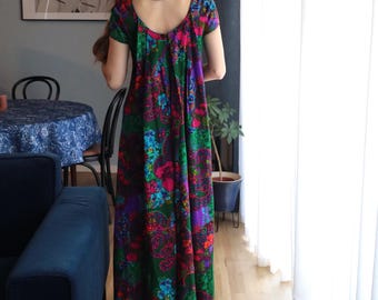 May include: A long, flowing dress with a vibrant floral pattern in shades of green, purple, pink, and blue. The dress has short sleeves and a scoop neckline. The fabric appears to be lightweight, suitable for warmer weather.