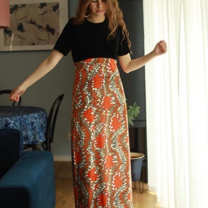 May include: A woman wearing a black short-sleeved top with a long, flowing skirt. The skirt is orange and white with a swirling pattern.