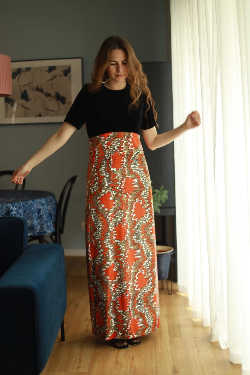 May include: A woman wearing a black short-sleeved top with a long, flowing skirt. The skirt is orange and white with a swirling pattern.