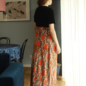 May include: A woman wearing a black short-sleeved top and a long orange and brown patterned skirt. The skirt has a swirling pattern.