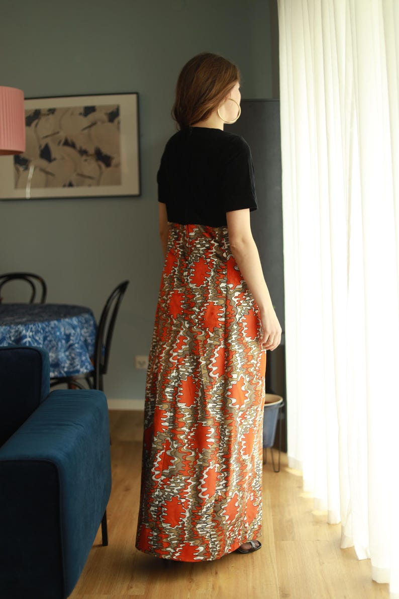 May include: A woman wearing a black short-sleeved top and a long orange and brown patterned skirt. The skirt has a swirling pattern.