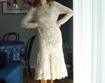 May include: A white lace dress with long sleeves and a flared skirt. The dress is worn with brown knee-high boots.