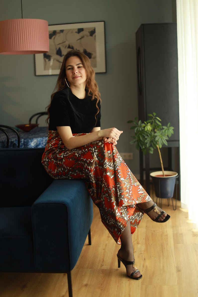 May include: A woman wearing a black velvet top and a long, flowing orange and brown patterned skirt sits on a blue velvet sofa. She is wearing black heels with gold accents.
