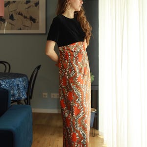 May include: A woman wearing a black velvet top with a long, orange and brown patterned skirt. The skirt has a swirling, abstract design.